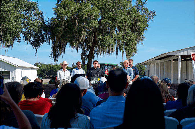 A small group stand at a podium outdoors, addressing an audience