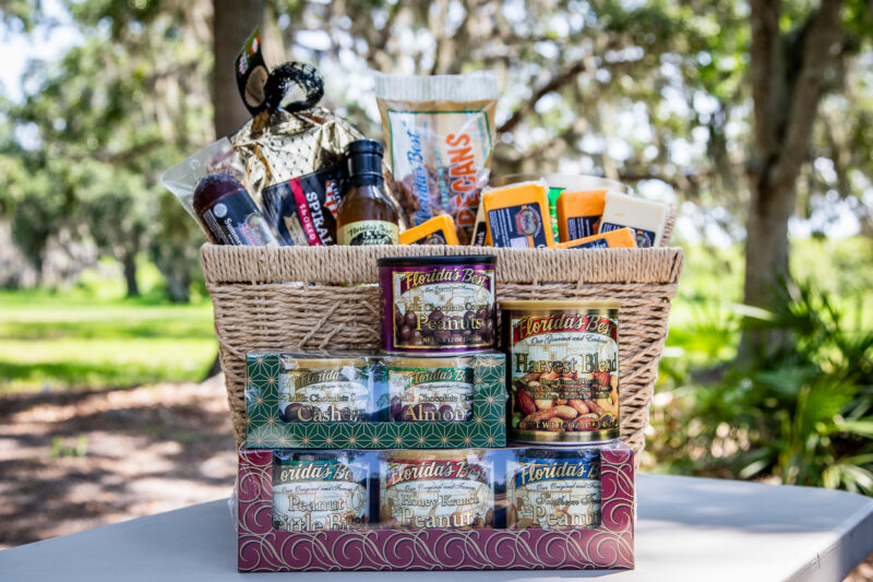 Woven basket and stacked boxes filled with Florida-made food products including nuts, cheese, vinegar, and specialty items