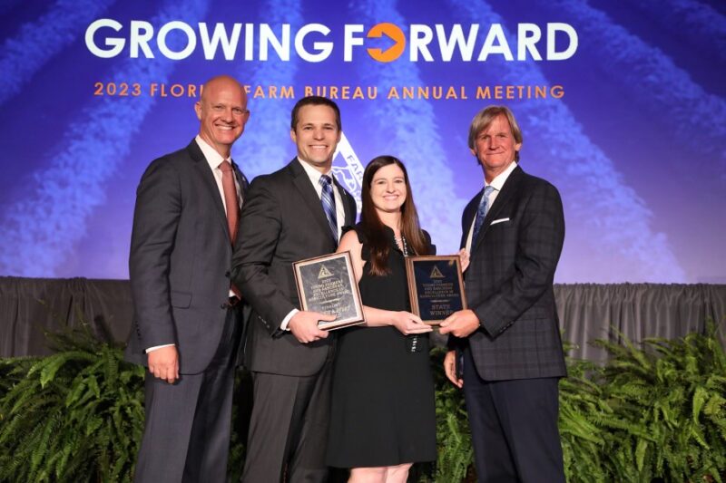 Four people standing on a stage holding award plaques during a Florida Farm Bureau annual meeting