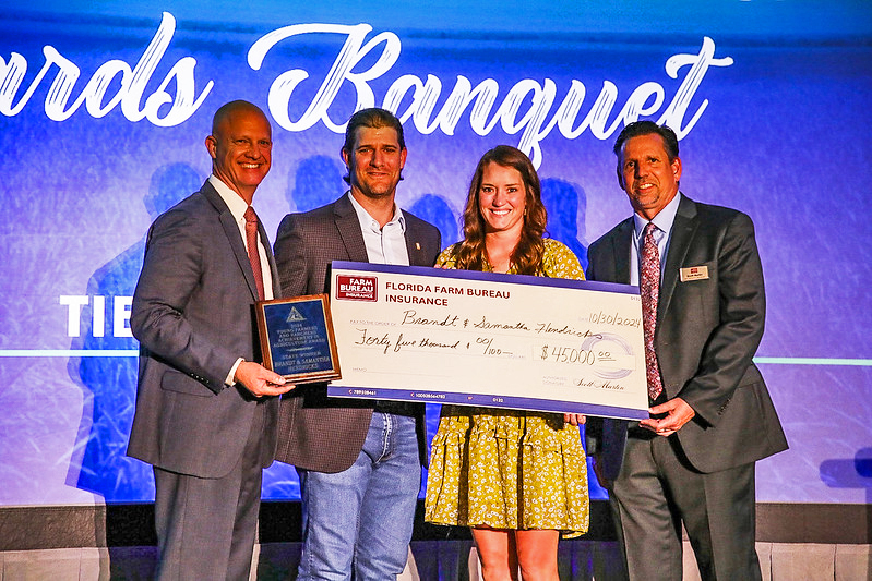 Brandt and Samantha Hendricks holding a presentation check while standing with Florida Farm Bureau representatives on stage during an awards presentation