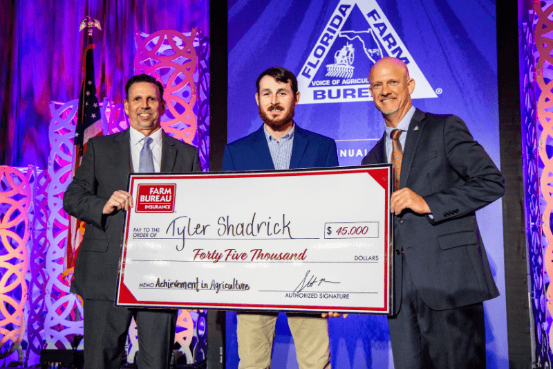 Tyler Shadrick holding a presentation check while standing with Florida Farm Bureau representatives on stage during an awards presentation