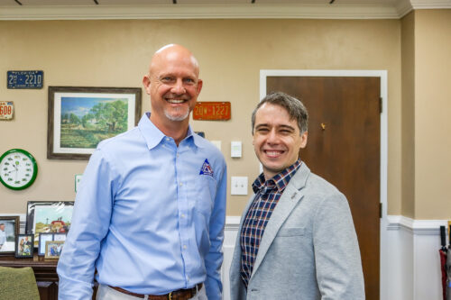 Florida Farm Bureau President Jeb S. Smith and Dr. Nathan Palardy stand side by side indoors, posing for a photo in an office setting with framed artwork and a door in the background.